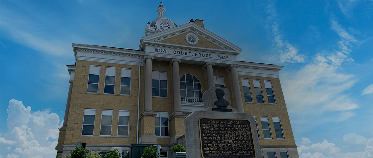 A historic courthouse building with a clock tower and a prominent portico, accompanied by a monument featuring a bust of Abraham Lincoln in the foreground.